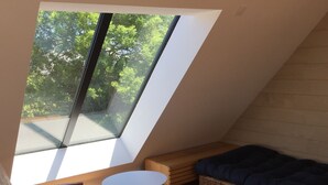 A small, sloped-roofed room with a wooden floor, a round white table, a cushioned bench, and a dark blue sofa. - Wooden house, close to beaches and dunes (Landéda)
