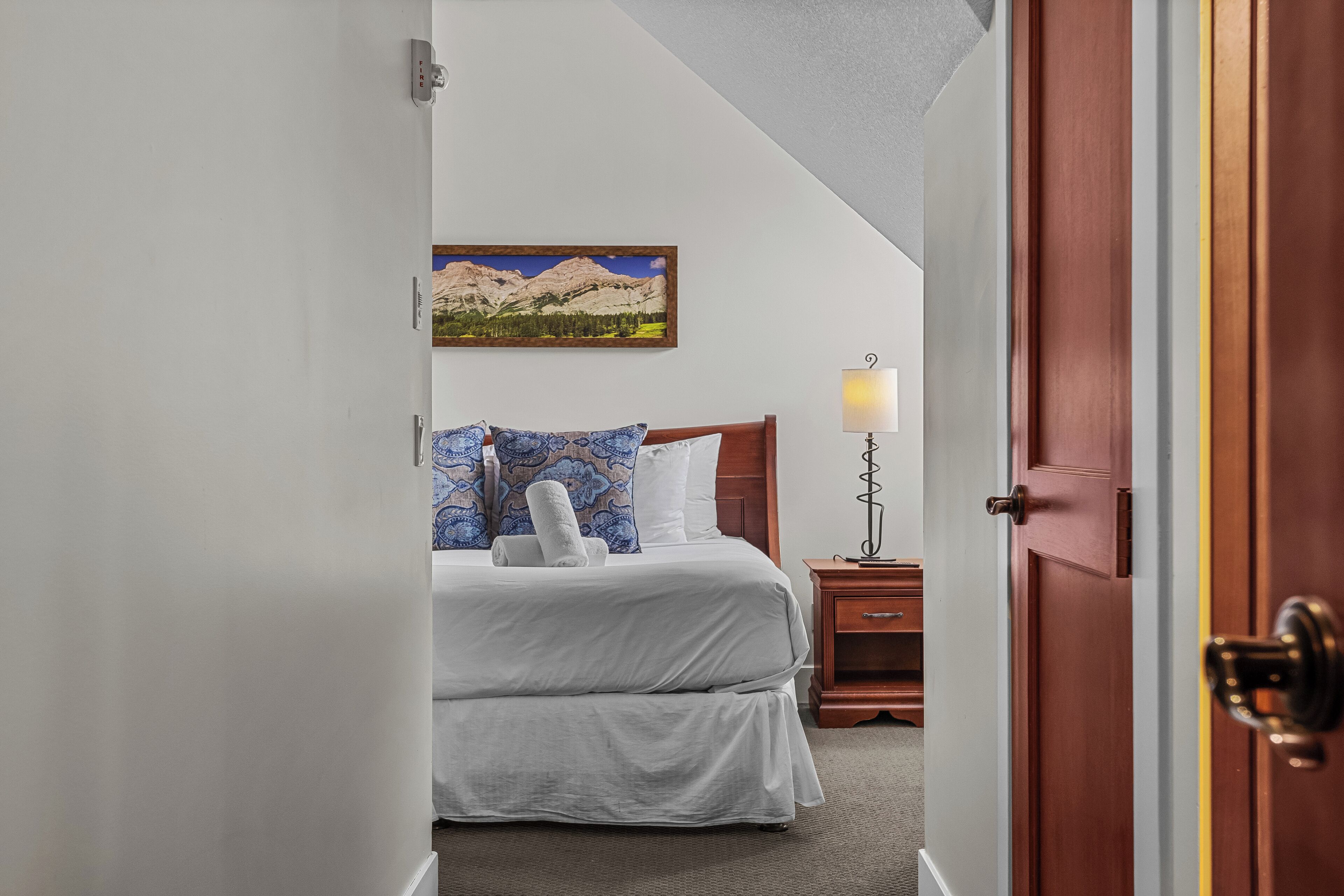 A hotel room with a bed, a nightstand, a lamp, and a painting on the wall.