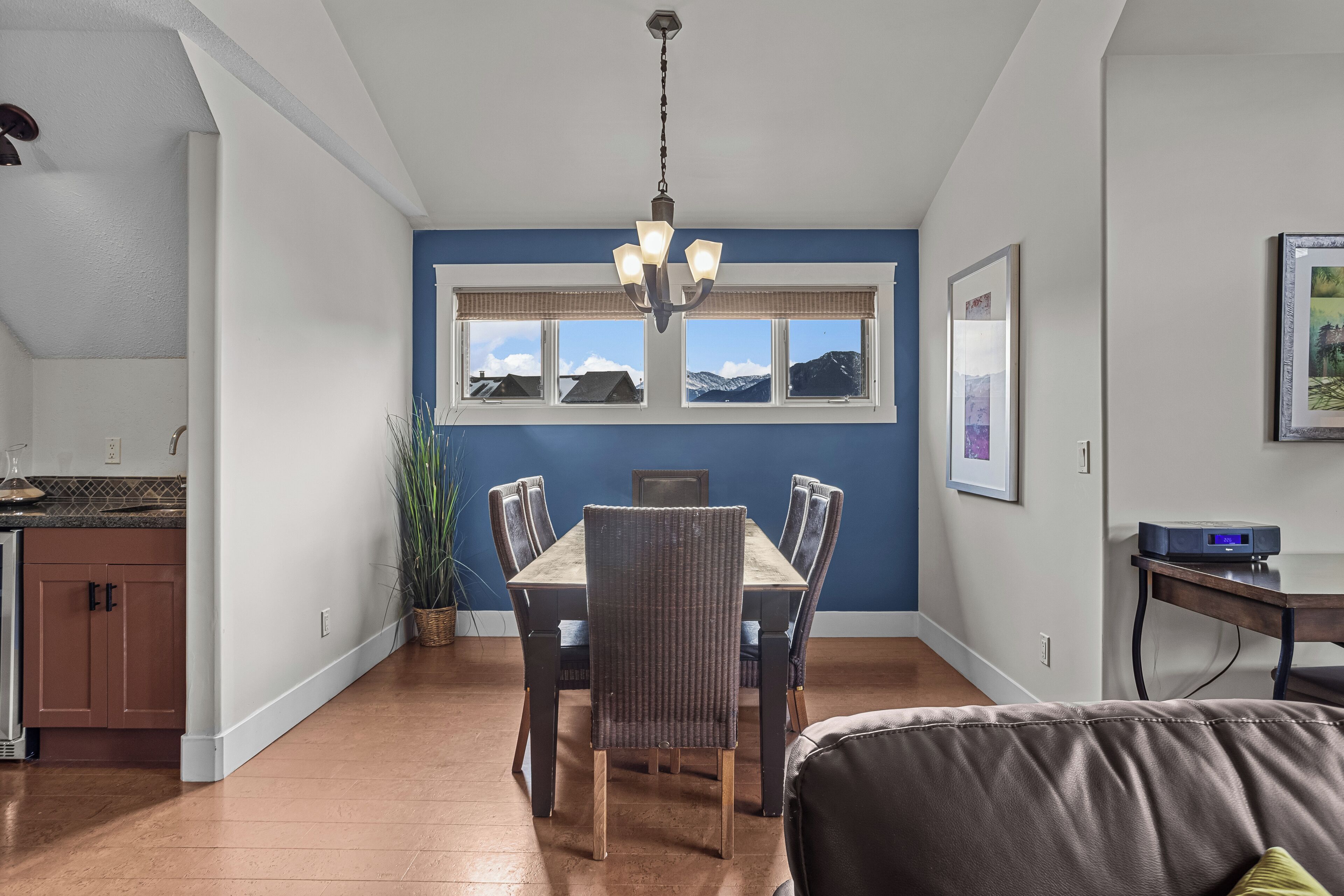 A dining area with a table and chairs, a chandelier, a window with a mountain view, and a kitchen area with cabinets and a countertop.