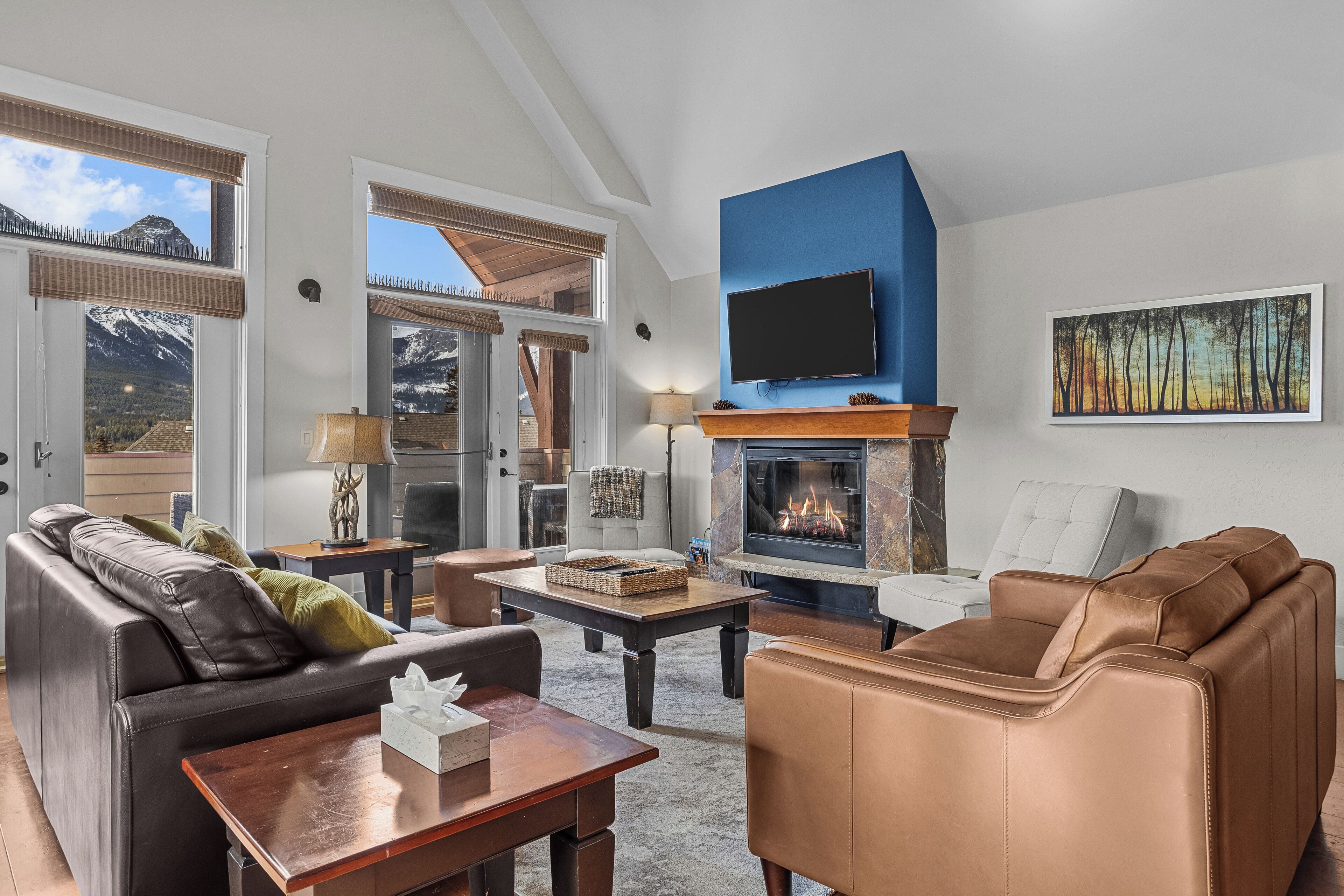 Een woonkamer met een open haard, leren banken, een televisie en uitzicht op de bergen.