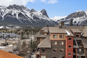 Un edificio de varios pisos con techo inclinado, ventanas grandes y vista a montañas nevadas.