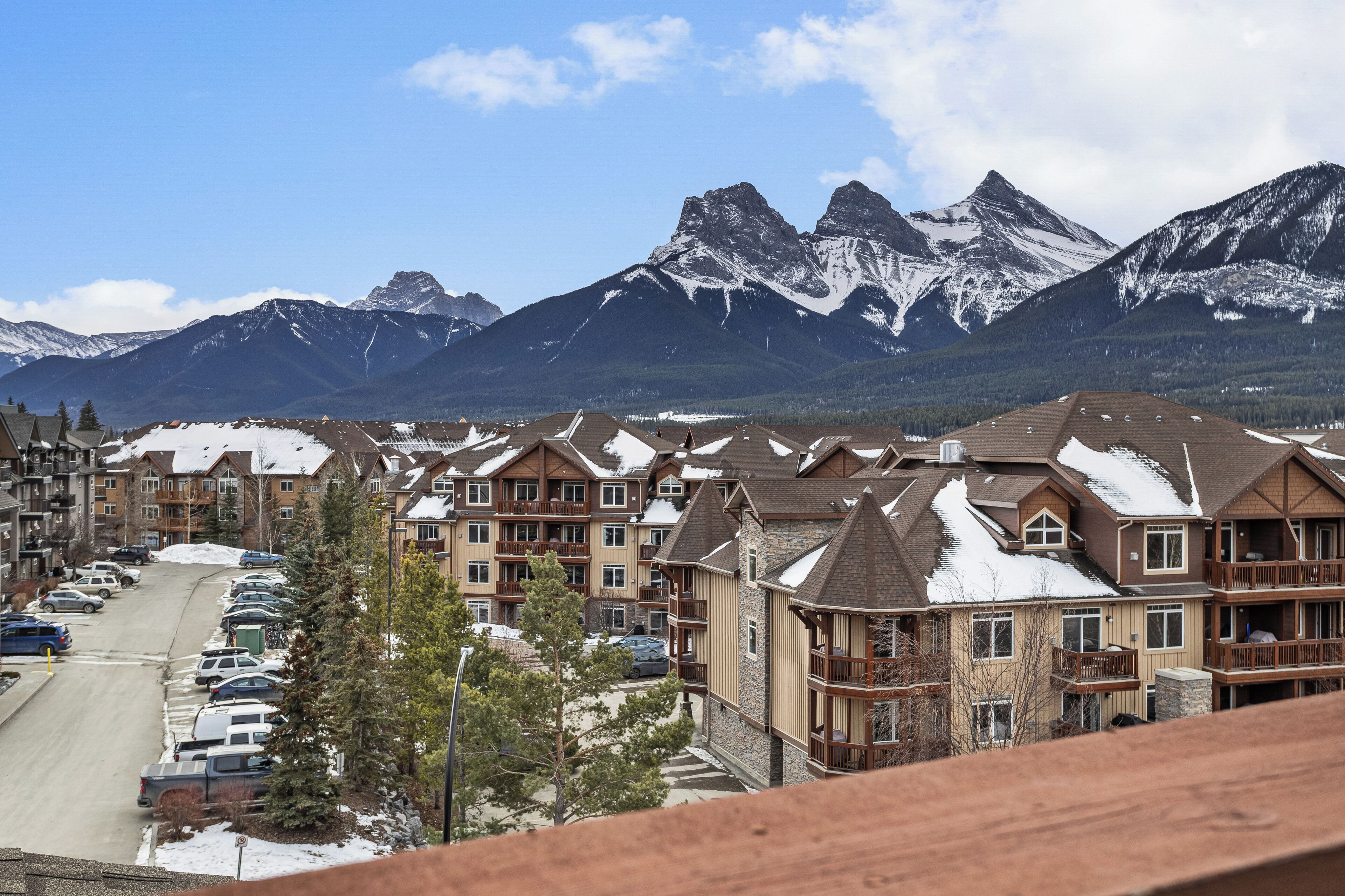 Un barrio residencial con edificios de varios pisos, un estacionamiento y montañas nevadas al fondo.