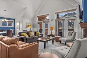 Ein geräumiges Wohnzimmer mit hohen Decken, einem Kamin und Blick auf Berge durch große Fenster.