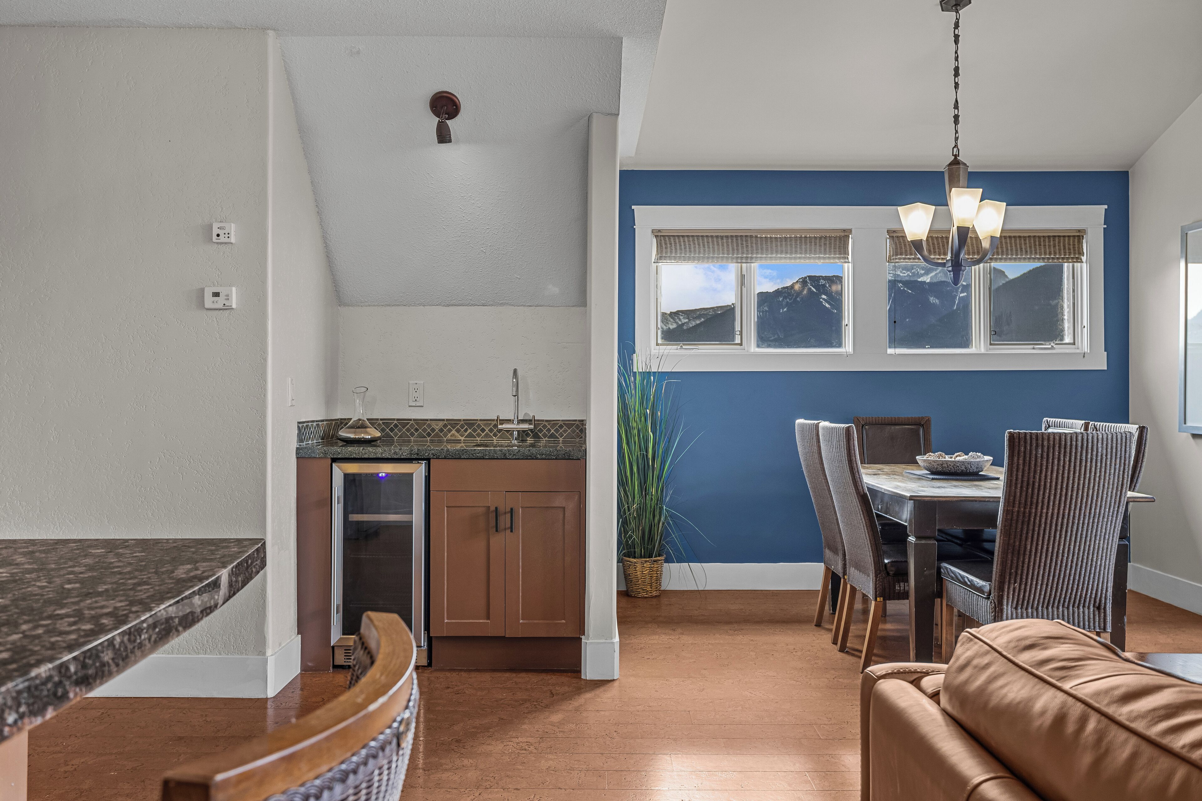 A kitchen with a built-in dishwasher, a dining area with a table and chairs, and a view of mountains through the windows.