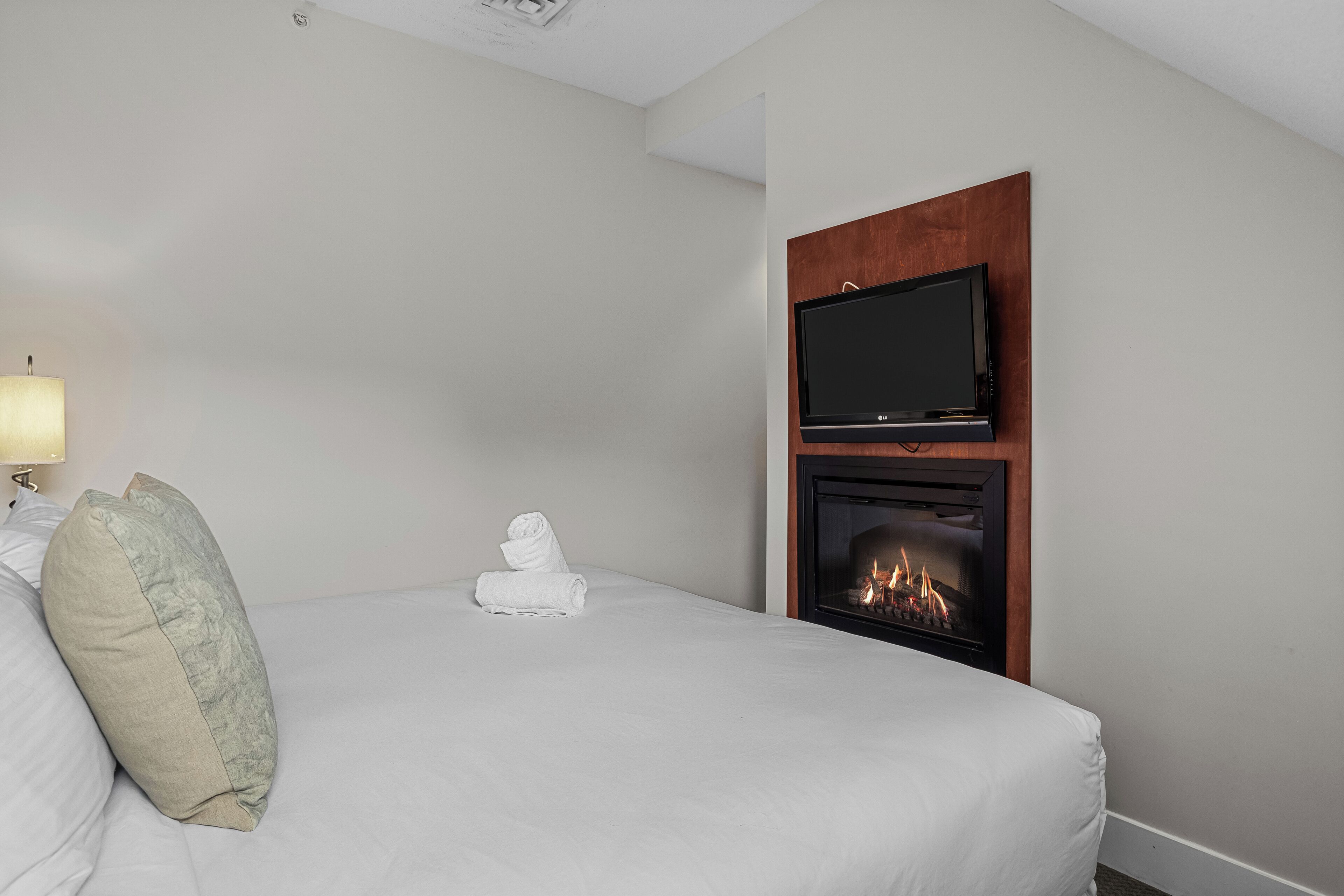 Une chambre d’hôtel avec un lit, un téléviseur à écran plat fixé au-dessus d’une cheminée et une lampe sur le côté gauche.