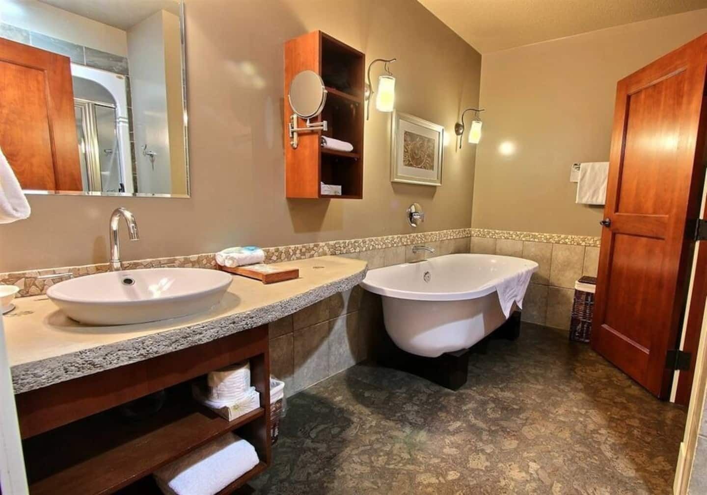 A bathroom with two sinks, a bathtub, a wooden vanity, a mirror, and a towel rack.