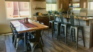 A modern kitchen with a dining area, featuring a wooden table, metal chairs, and pendant lights. - Moab Village Luxury Retreat Gorgeous views, PVT Hot Tub, 3 STE, 3.5 BTH, 1.5 KT (Moab)