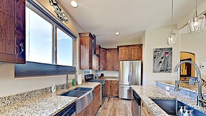 A modern kitchen with granite countertops, stainless steel appliances, wooden cabinets, and a large window providing natural light. - Moab Village Luxury Retreat Gorgeous views, PVT Hot Tub, 3 STE, 3.5 BTH, 1.5 KT (Moab)