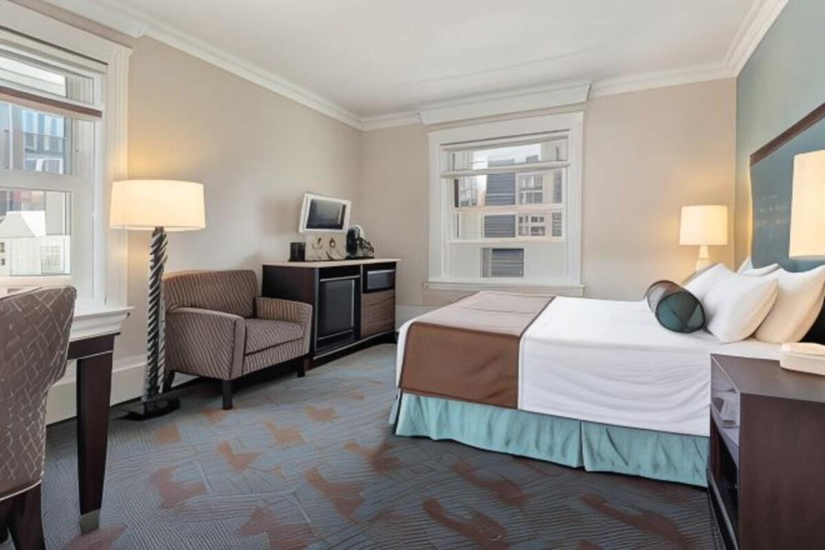 A hotel room with a bed, a desk, a chair, a TV, and a window.