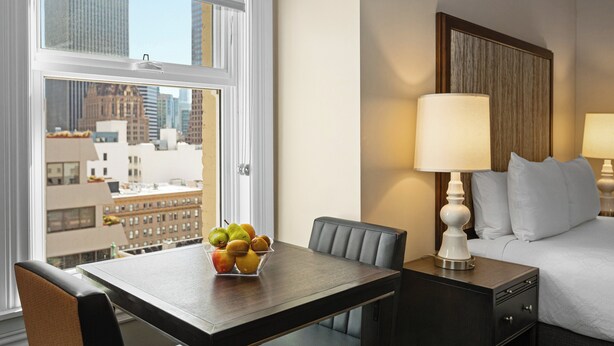 A hotel room with a dining table, a bowl of fruit, a bed with white bedding, and a nightstand with a lamp. - WorldMark San Francisco (San Francisco)