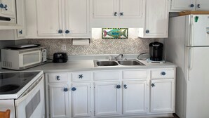 Una cocina con armarios blancos, microondas, tostadora, cafetera y refrigerador.
