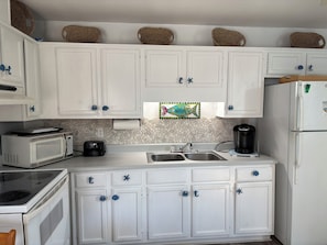 A kitchen with white cabinets, a microwave, a toaster, a coffee maker, and a refrigerator.