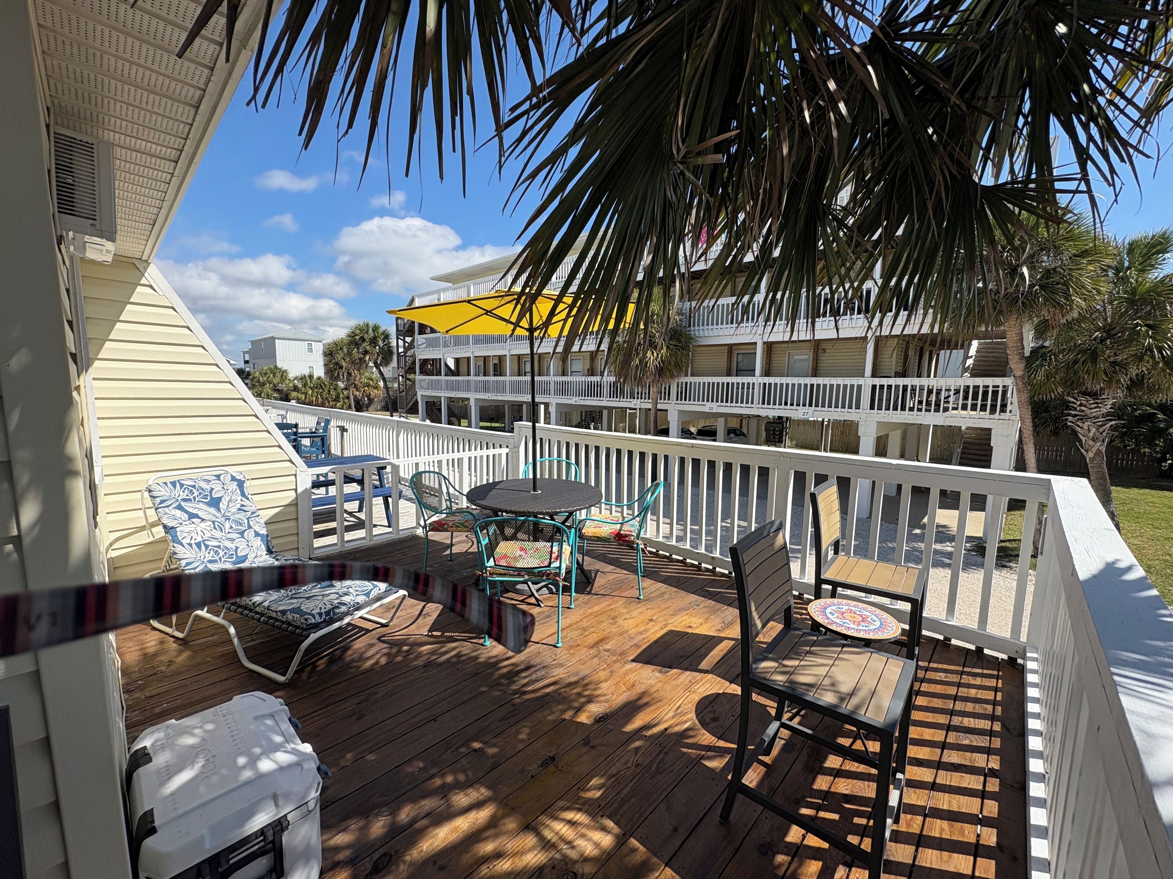 A wooden deck with outdoor furniture, a yellow umbrella, and a white railing.