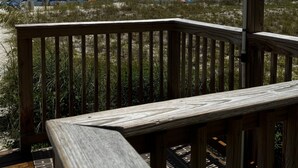 Una terraza de madera con barandilla de metal que da a una playa con sombrillas y una bandera.