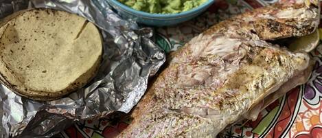 A whole fish on a colorful plate with foil wrapping and a bowl of guacamole.