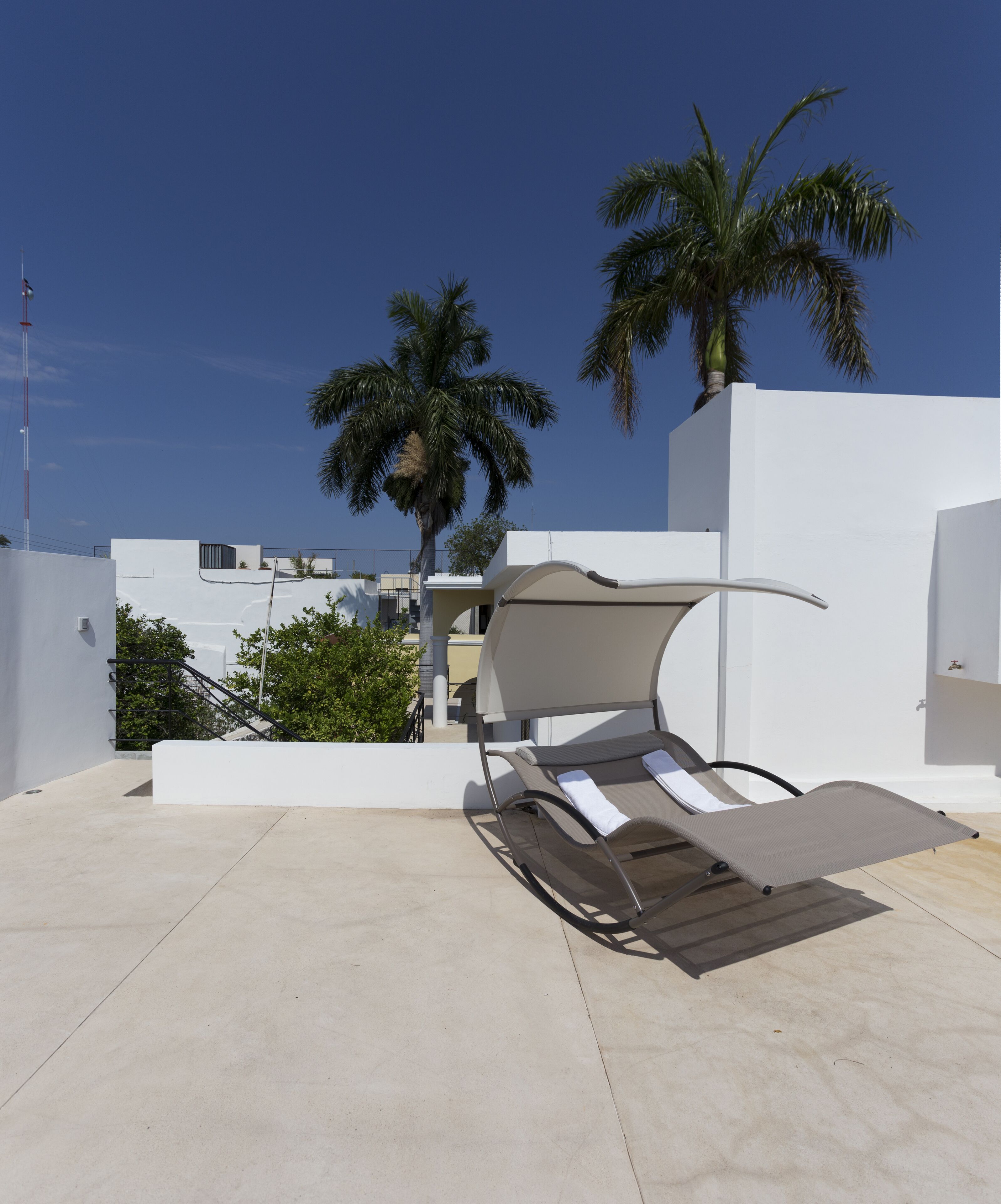 A modern outdoor lounge area with a reclining chair, a concrete floor, and a white building in the background.