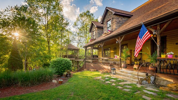 Een rustieke houten hut met een veranda, stenen muren en een Amerikaanse vlag.