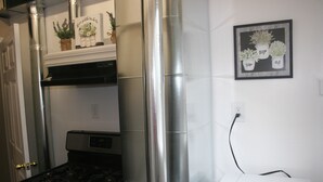 A kitchen with a stove, microwave, and a wall-mounted vent. There are potted plants on the wall and a framed picture above the microwave. - Layton's Loft (Manti)