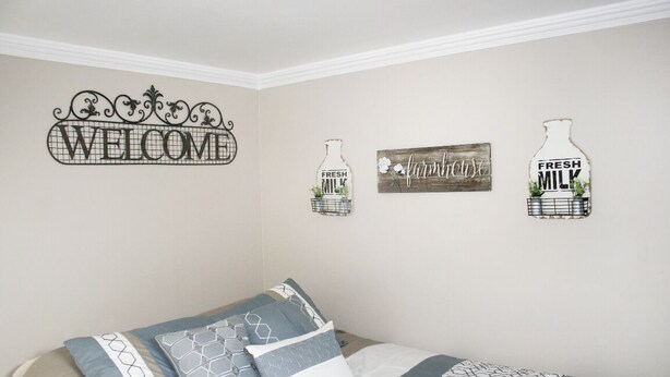 A bedroom with a bed, pillows, and wall decorations including a 'WELCOME' sign, a 'FRESH MILK' sign, and a 'farmhouse' sign. - Layton's Loft (Manti)