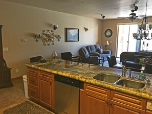 A kitchen with a granite countertop, wooden cabinets, a dishwasher, and a dining area with a chair and table. - Luxury Condo in Brian Head,  Beautiful Amenities,  Easy Walk/Ski To Slopes (Brian Head)