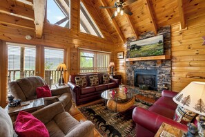 A log cabin interior with a fireplace, wooden beams, a sofa, and a dining table.