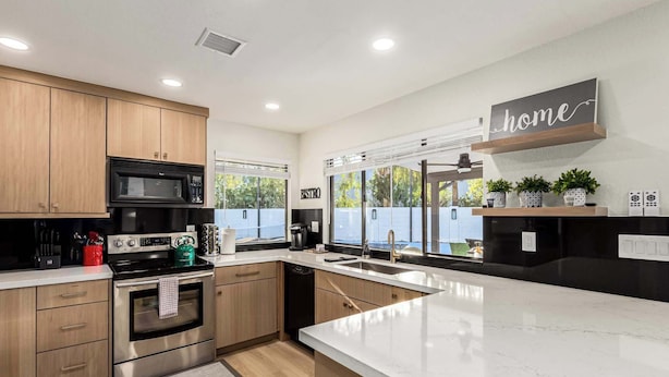 A modern kitchen with wooden cabinets, stainless steel appliances, a large island, and a view of the outdoors. - Private Luxury 6BR Resort: Pool, Pickleball, Oasis (Scottsdale)