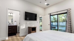 A bedroom with a large bed, a TV mounted on the wall, a bathroom with a mirror and sink, and a sliding glass door leading to a backyard. - Private Luxury 6BR Resort: Pool, Pickleball, Oasis (Scottsdale)