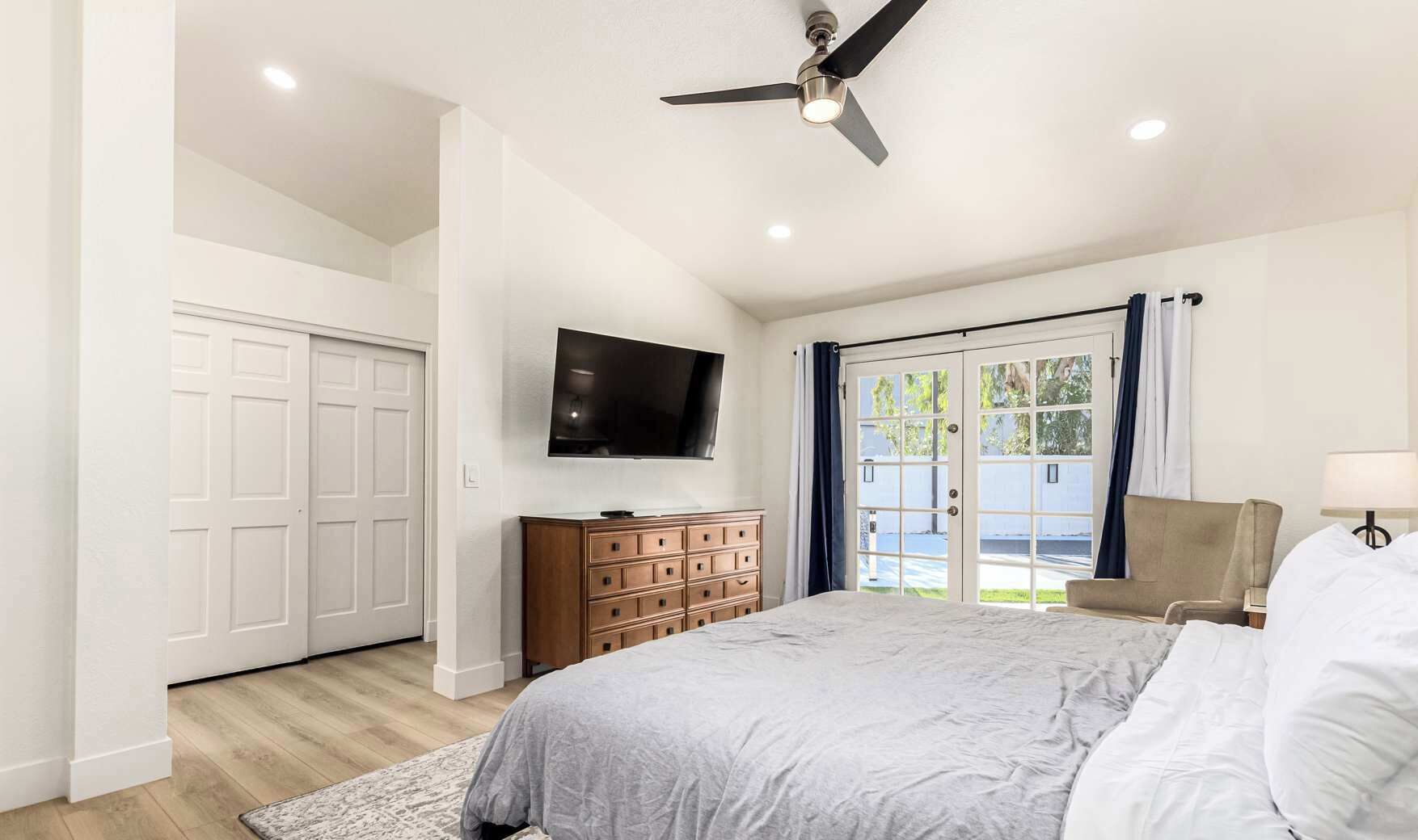 A bedroom with a bed, a dresser, a television, and a sliding glass door to the outside.