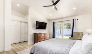A bedroom with a bed, a dresser, a television, and a sliding glass door to the outside.