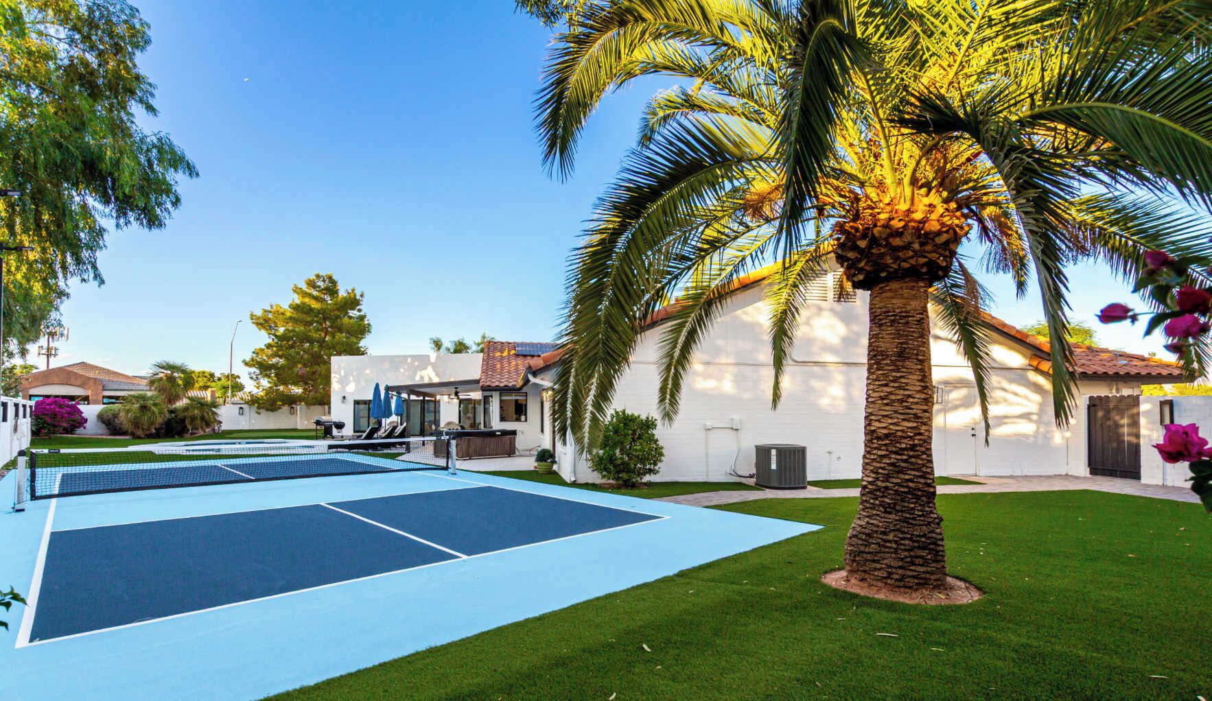A tennis court with a net, surrounded by a well-maintained lawn and palm trees.