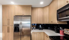 A modern kitchen with stainless steel appliances, wooden cabinets, and a black microwave.