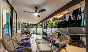 Une terrasse extérieure avec des meubles en osier, un ventilateur de plafond et une piscine.