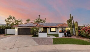 Una casa de una sola planta con techo de tejas, paneles solares, garaje y césped cuidado.