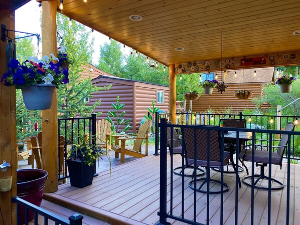 A wooden deck with outdoor furniture, potted plants, and a wooden cabin in the background.
