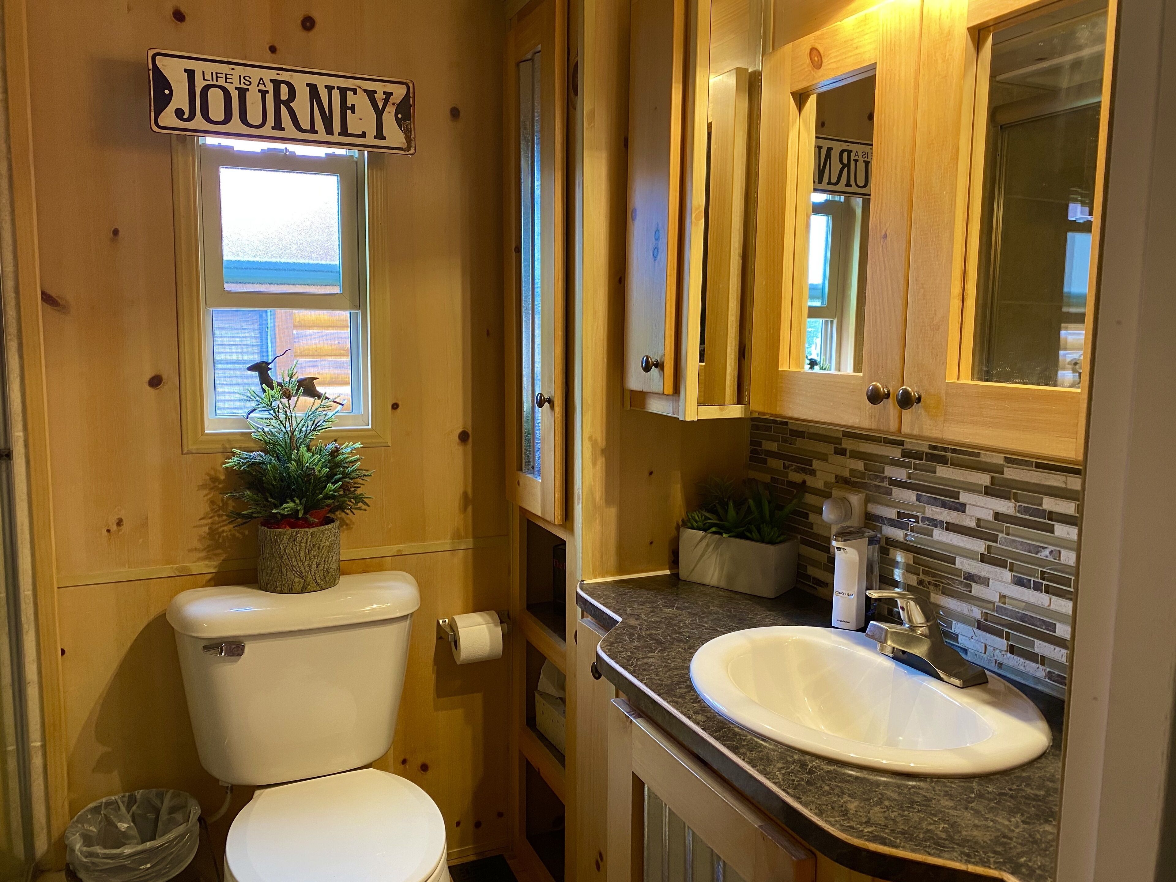 Une salle de bain en bois avec des toilettes, un lavabo et une pancarte sur laquelle est écrit : « La vie est un voyage ».