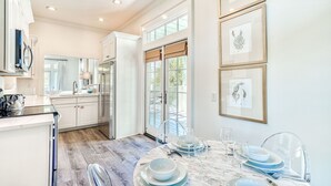 A modern kitchen with white cabinets, a stainless steel refrigerator, and a dining area with a marble table set for four.
