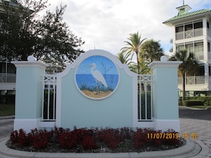 Un bâtiment orné d’une fresque murale circulaire représentant un oiseau sur une plage, le tout entouré d’un mur bleu clair et de piliers blancs.