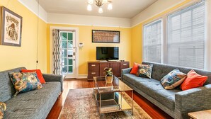 A living room with two sofas, a coffee table, a TV, and a chandelier. - Riverbend Gem in Historic Carrollton Uptown  (New Orleans)
