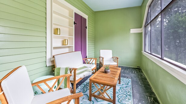 A porch with a ceiling fan, a white sofa, two wooden chairs, a small table, and a patterned rug. - Riverbend Gem in Historic Carrollton Uptown  (New Orleans)