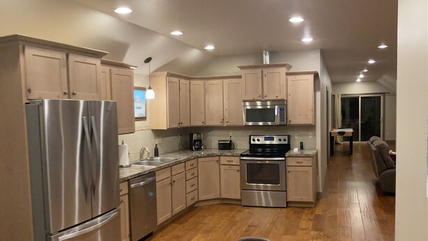 A modern kitchen with stainless steel appliances, wooden cabinets, and a dining area with a wooden table and chairs.