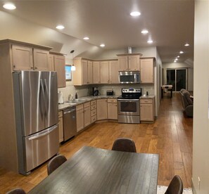 A modern kitchen with stainless steel appliances, wooden cabinets, and a dining area with a wooden table and chairs.