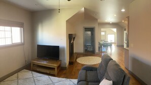 A spacious living room with a flat-screen TV on a wooden stand, a grey sofa, and a patterned rug.