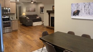 A modern kitchen with stainless steel appliances, a dining area with a wooden table and chairs, and a living room with a sofa and fireplace.