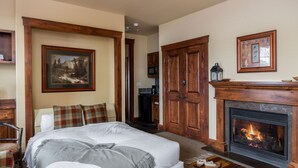 Ein Schlafzimmer mit einem großen Bett, einem Kamin, Holztüren und einem gerahmten Bild an der Wand.