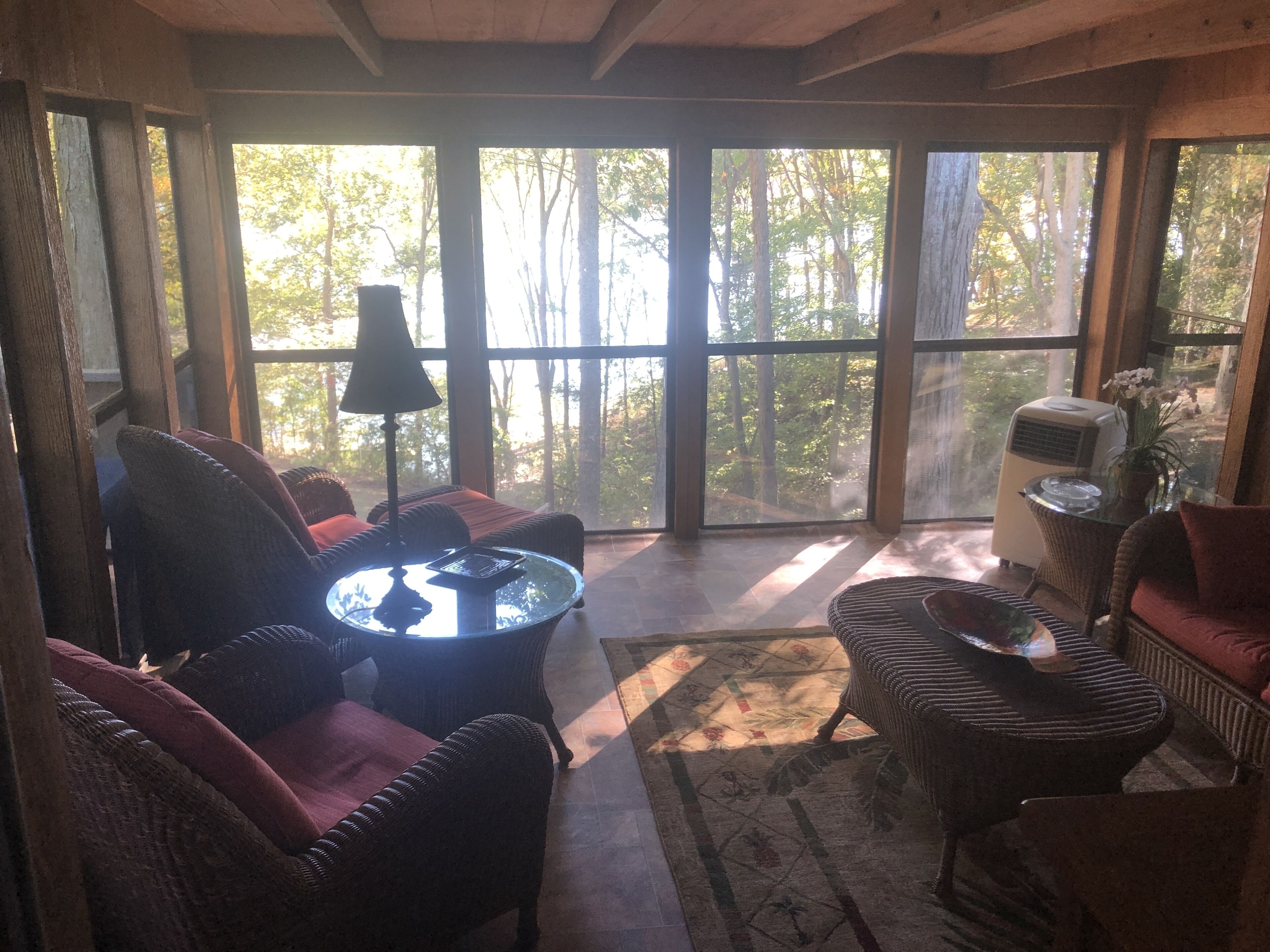 A spacious room with large windows, wicker furniture, and a central glass table.