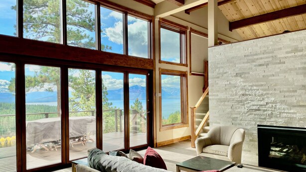 Amplia sala de estar con ventanas grandes que ofrecen una vista panorámica de montañas y un lago.