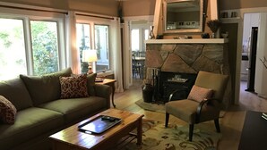 A cozy living room with a sofa, armchair, coffee table, fireplace, and large windows. - The Kenwood House - A Place to Stay
Your Wine Country Oasis in Sonoma Valley (Kenwood)