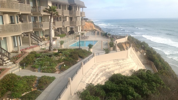 Un hotel frente a la playa con piscina, una escalera que lleva a la playa y vista al océano.