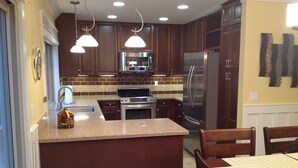 Cocina con armarios de madera, electrodomésticos de acero inoxidable e iluminación colgante.