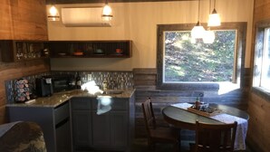 A cozy cabin-style kitchen with a central island, wooden cabinetry, and a dining area with a table and chairs. - Rustic luxury deep in the heart of Texas  (Hamilton)